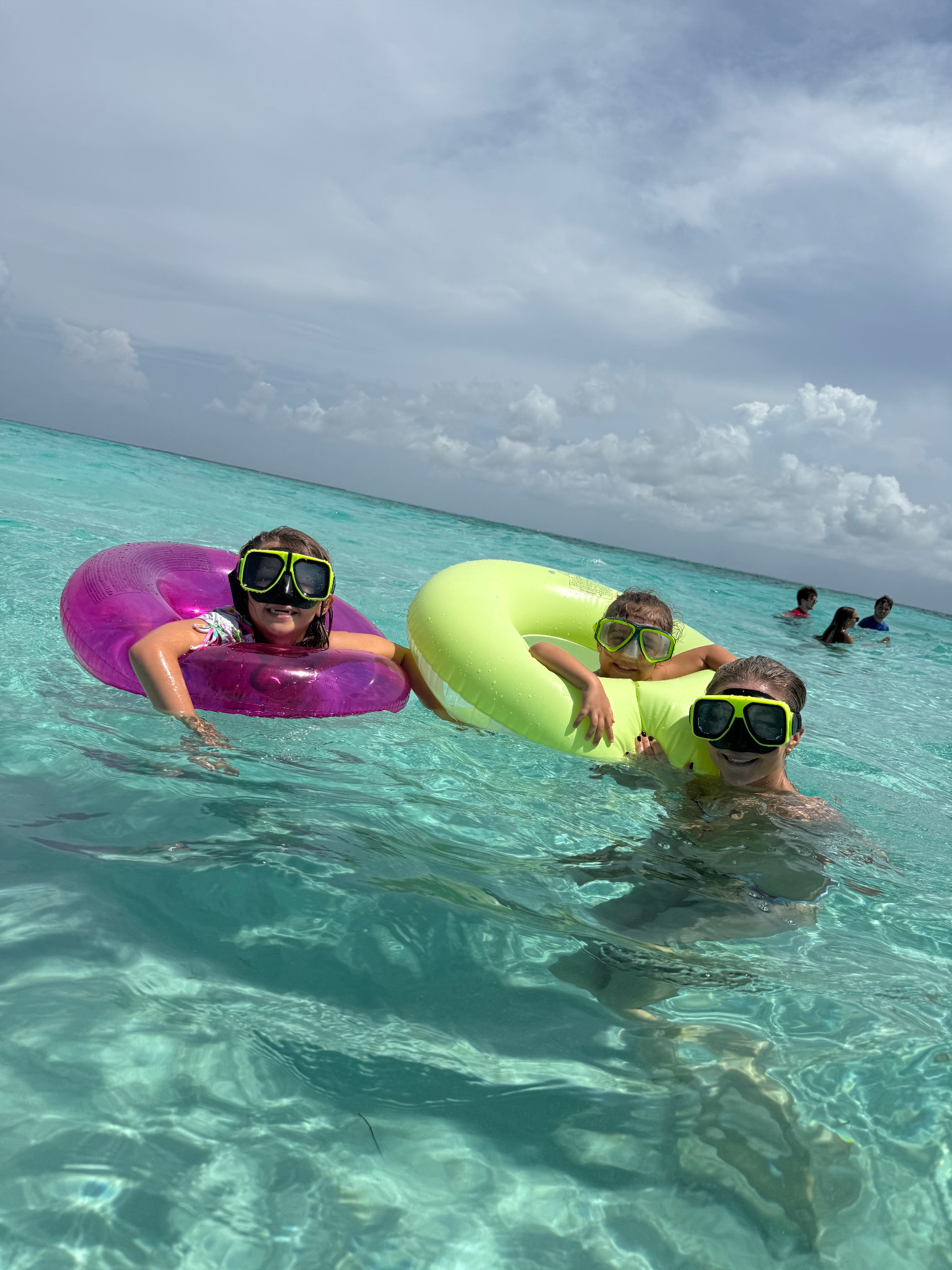 A parent and two children in dive masks and floats enjoying clear, calm shallow turquoise water in Grand Cayman.