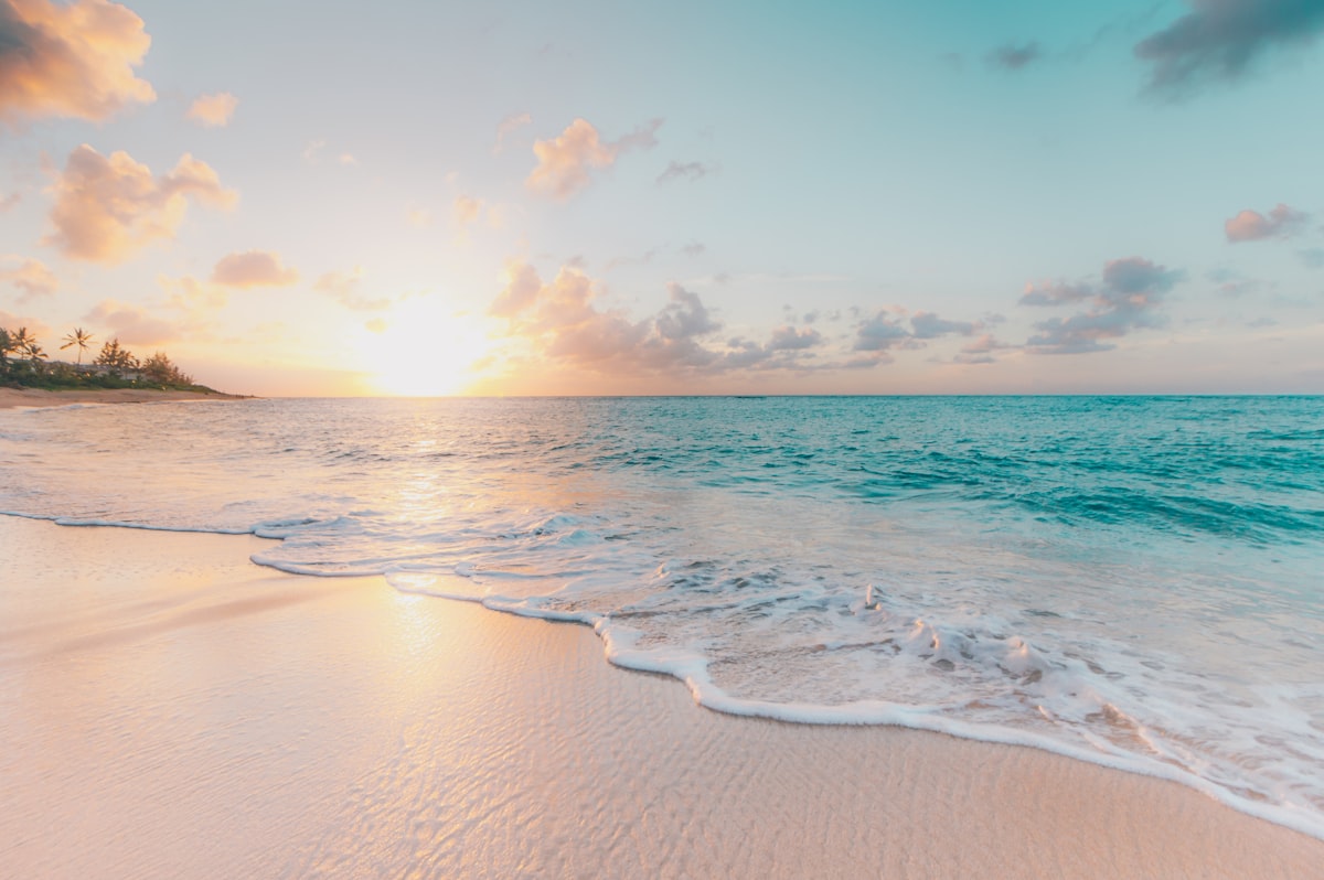 A calm Caribbean beach at golden hour with turquoise water and soft surf