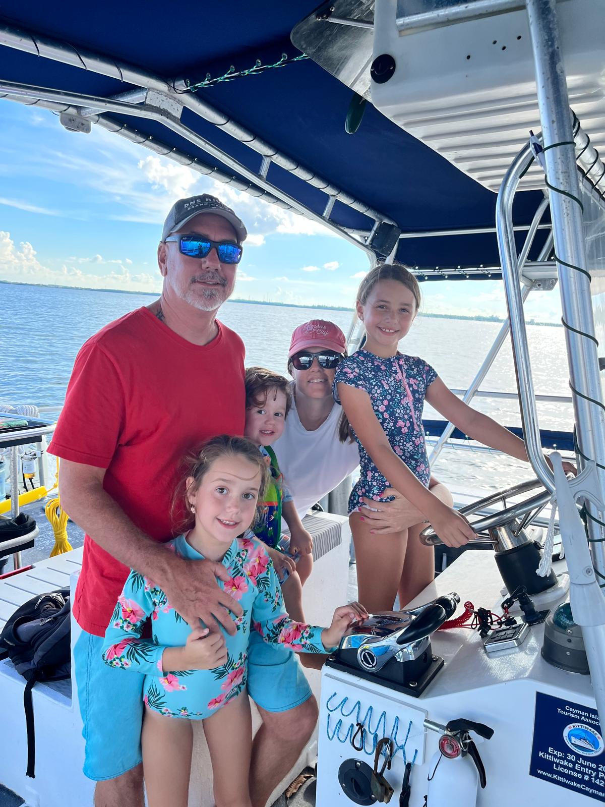 A family gathered at the helm of a DNS Diving boat on open water, one of the kids holding the wheel