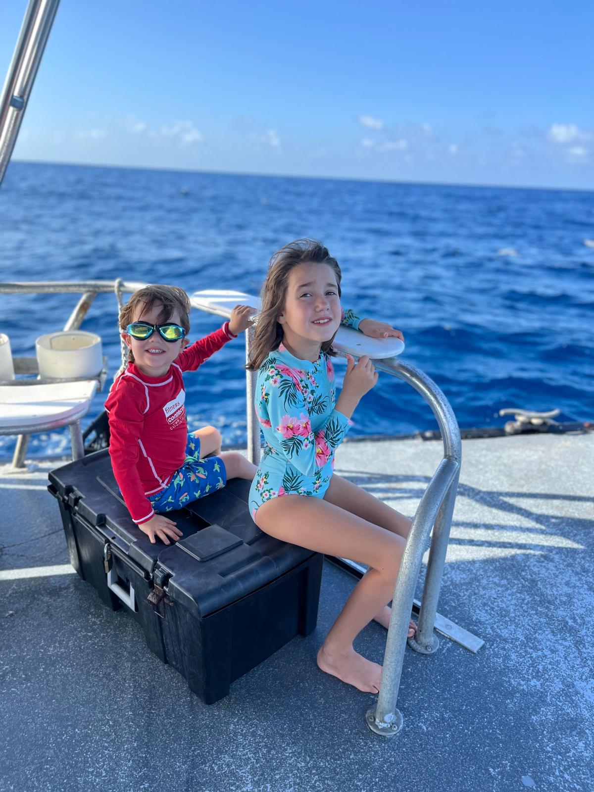 Two kids relaxing on the stern deck of a DNS Diving boat with deep blue water behind them