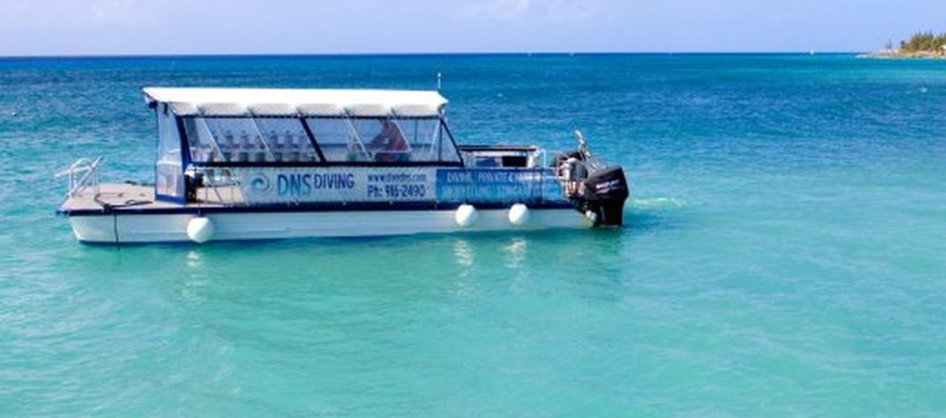 The DNS Diving boat Viewfinder on clear turquoise Grand Cayman water, DNS Diving branding on the hull